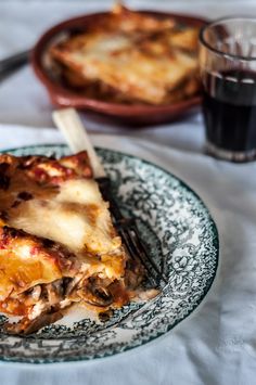 a slice of lasagna on a plate next to a glass of black wine