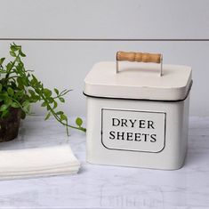 a white box with a wooden handle on top of a table next to a potted plant