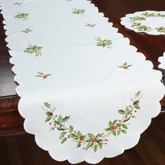 the table cloth is decorated with holly and red berries on white linen, along with matching placemats