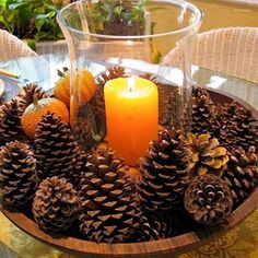 a candle is lit in a bowl with pine cones and oranges on the table