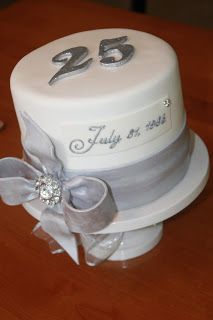 a white cake with silver ribbon and number twenty five on the top, sitting on a wooden table