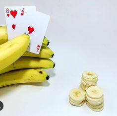 a stack of bananas with playing cards next to them on a white surface, surrounded by small stacks of banana slices