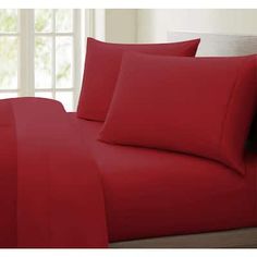 a bed with red sheets and pillows on it