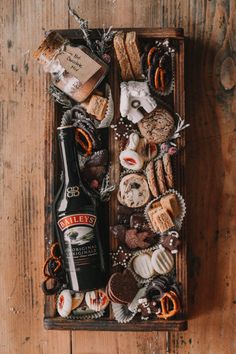 a wooden box filled with lots of different types of cookies and pastries next to a bottle of beer