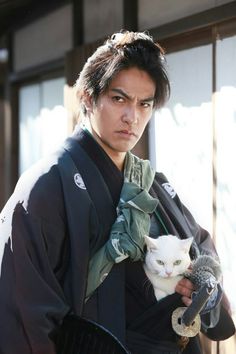 a man holding a white cat in his hand and wearing a kimono over his shoulder