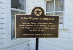 a sign in front of a white house that says john wayne birth place on it