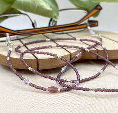 Dramatic and bohemian eyeglass necklace chain in matte purple and rainbow tones made with Preciosa Czech crystal seed beads and purple cubic zirconia charms.      Paired with beautiful and delicate purple charms, this handmade eyeglass chain will definitely create a unique look. This eyeglass lanyard is made on strong quality beading wire with silver plated wire guardians that protect the eyeglass holder grips. The necklace is ended with spring clasps that hold the eyeglass grips and they can be easily removed to transform the necklace into a mask holder. FREE Shipping for additional items  ~ All items are beautifully packed ready to give as a gift and carefully wrapped up to ensure a safe delivery.   ~ The environment is very important for us therefore, in order to reduce waste, we will p Adjustable Lavender Beaded Necklaces, Adjustable Purple Glass Beaded Necklaces, Handmade Purple Glass Beaded Necklaces, Adjustable Purple Glass Glasses Chains, Purple Glass Glasses Chains As Gift, Beaded Sunglasses Chain, Purple Charms, Eyeglass Chain Holders, Glasses Lanyard