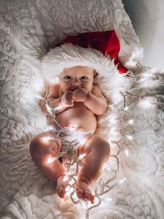 a baby in a santa hat is laying on a blanket with christmas lights around it