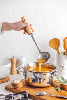 a person pouring liquid into a pot on top of a wooden cutting board next to utensils