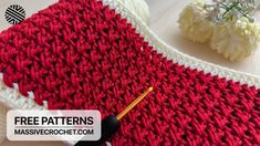 a crocheted red and white blanket with a needle in the middle next to it