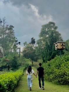 two people holding hands walking down a path in the middle of a lush green field