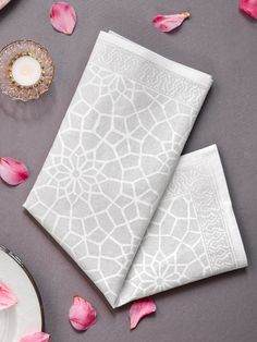 two white napkins sitting on top of a table next to pink flowers and plates