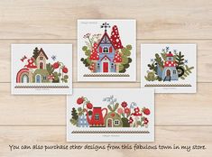 four cross stitch cards with houses and trees in them on a wooden surface, one has a red house