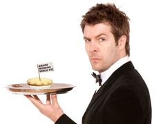 a man in a tuxedo holding a cake on a plate with a sign