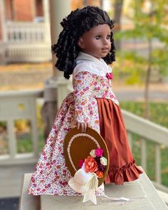 a doll is sitting on top of a table with a plate in her hand and wearing a flowered dress