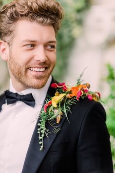 a man in a tuxedo smiles at the camera while wearing a boutonniere