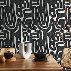 a wooden table topped with two vases next to a wall covered in black and white designs