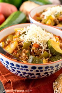 two bowls filled with chili and veggies next to bread on a red cloth