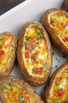 several baked potatoes in a white dish on a wooden table