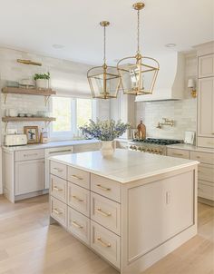 a large kitchen with white cabinets and gold hardware on the island countertop, along with two hanging lights