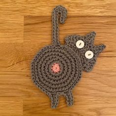 a crocheted cat with two eyes on it's back sitting on a wooden floor