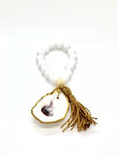 The Lagoon is yet another versatile style within the Boho collection. Featuring all-natural wood beads, each piece is connected at the base by an 18k gold gilded oyster shell, and a handcrafted tassel. Easily hung from a door handle to designate a particular room, directly on the wall by nail or hook, or from the corner of your favorite framed photo - you will have no trouble finding the perfect spot for this style to be displayed in your home. Bead Size: 20mm/Approx 1", Overall Length: 8-9" Han Oyster Shell, Gold Gilding, Versatile Style, Door Handle, Wood Beads, The Wall, Natural Wood, Shells, 18k Gold