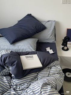 an unmade bed with blue and white striped sheets, pillows and a book on it