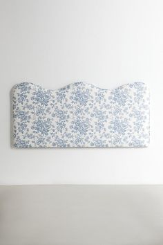 a white bed with blue and white flowers on it's headboard, against a white wall