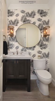 a bathroom with palm leaf wallpaper and a round mirror above the sink, along with a toilet