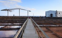 a wooden walkway leading to the ocean with people walking on it and an artistic building in the background