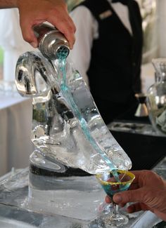 someone is pouring something into a glass on top of an ice - like table with other people in the background