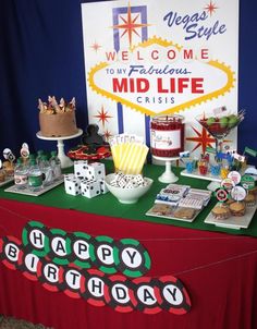 a red table topped with lots of cakes and desserts next to a sign that says happy birthday