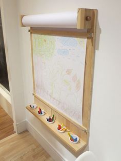 a white toilet sitting next to a wall mounted drawing board with three cups on it