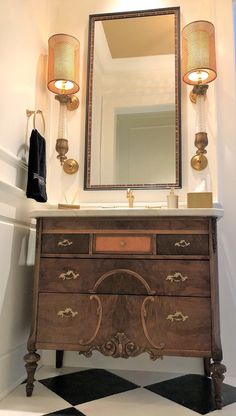 a bathroom vanity with a mirror above it and two lamps on the wall next to it