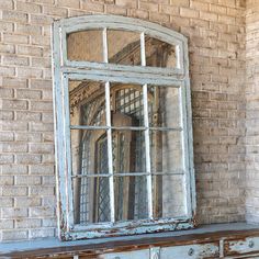 an old window sitting on top of a wooden dresser next to a brick wall with a mirror over it