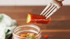 a person is holding a pickle over a jar filled with sauce and other ingredients