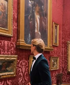 a man in a tuxedo looking at some paintings on the wall behind him