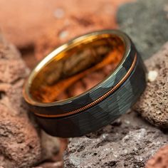 a gold and black wedding ring sitting on some rocks