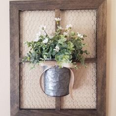 a metal bucket with flowers in it hanging on a wall above a chicken wire frame