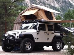 a white jeep parked in front of a tent on the side of a forest road