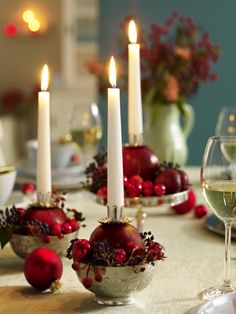 the table is set for christmas with candles and ornaments in bowls, wine glasses and plates