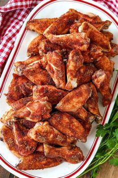 chicken wings on a white plate with parsley next to it and a red and white checkered napkin