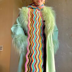 a woman wearing a green coat with multicolored crocheted stripes on it