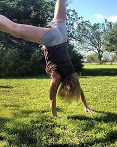 a person doing a handstand in the grass with their arms stretched out and legs bent