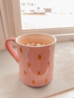 a pink coffee mug with gingerbreads on it sitting in front of a window