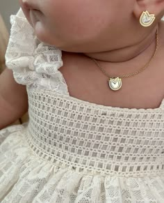 a baby wearing a white dress and gold necklace with two hearts on it's chest