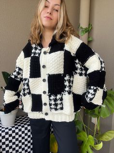 a woman standing in front of a potted plant wearing a black and white sweater