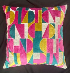 a pink and yellow pillow with geometric shapes on the front, sitting on a black background