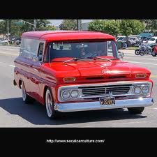 an old red truck is driving down the street with other cars in the back ground