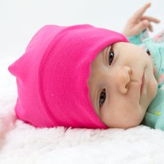 a baby wearing a pink hat laying on top of a white blanket